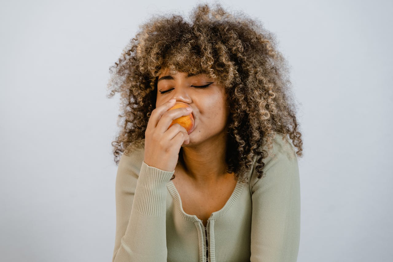 Woman Wearing Long Sleeve Shirt Eating a Fruit